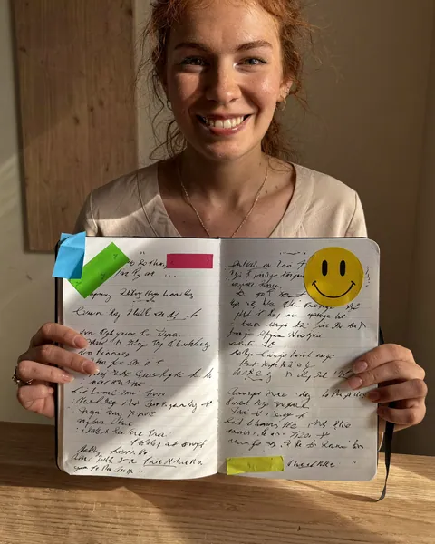 Mujer sonriendo mientras sostiene su cuaderno abierto